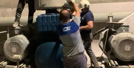 Uzman bir teknisyen, endüstriyel blower sisteminin parçalarını dikkatlice incelediği bir atölyede çalışıyor. Görselde teknisyenin elinde tuttuğu blower pervanesi ve yanında açık motor kısımları görülebilir, bu da periyodik bakımın detaylı bir süreç olduğunu vurgular.